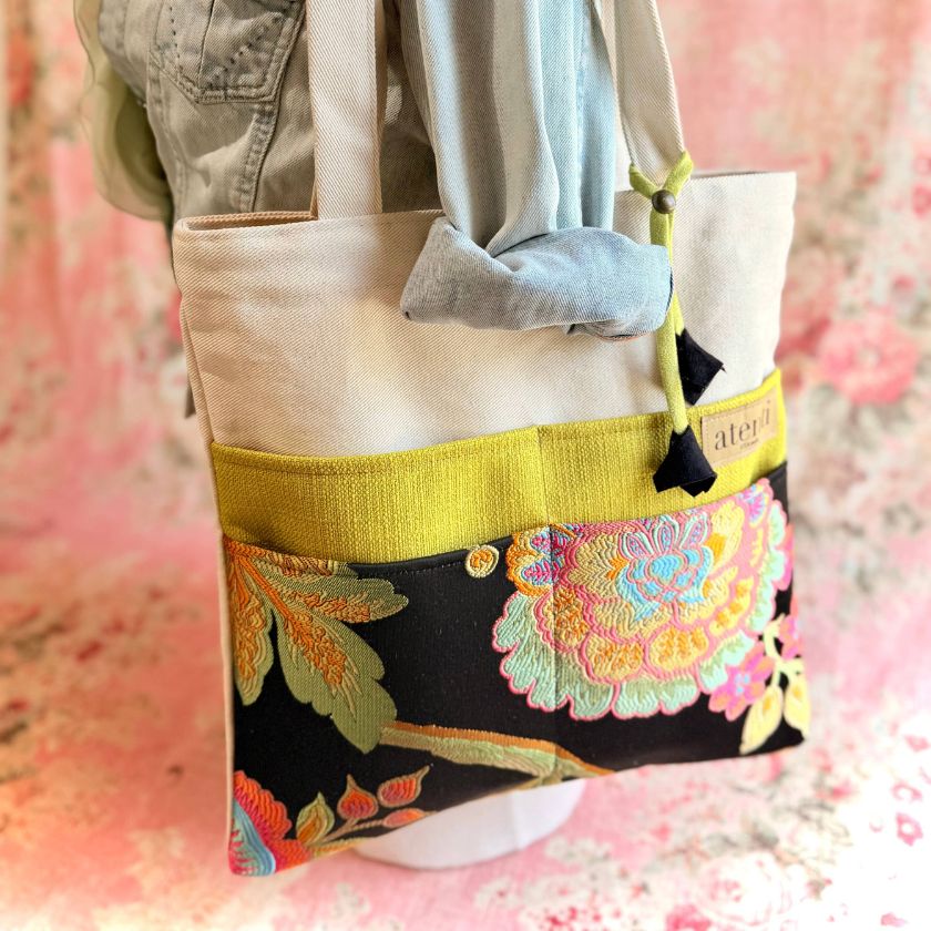 Colorful atenti knitting tote bag with floral design and yellow trim on a pink floral background
