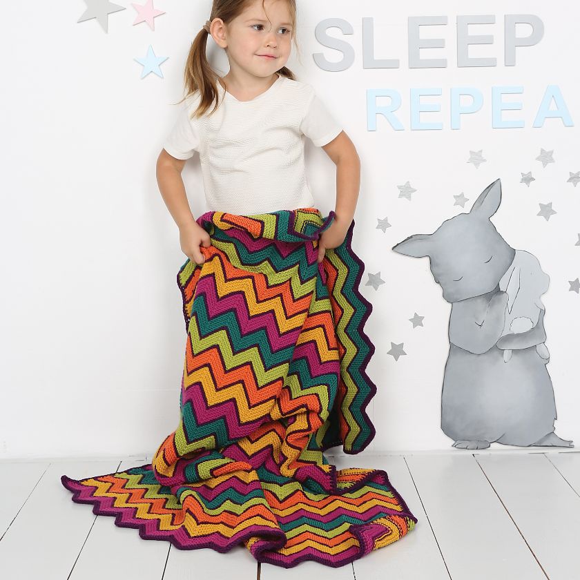 Child holding the Zita Baby Blanket in front of a wall that says Sleep Repeat