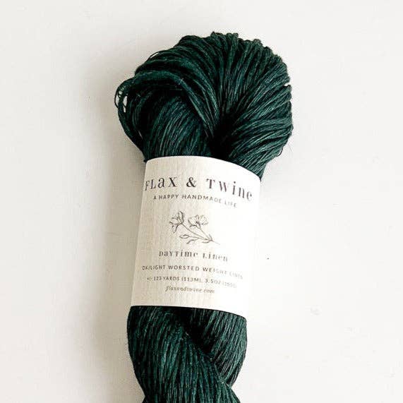 Ball of Flax & Twine Daytime Linen yarn in dark green with a label on a light background