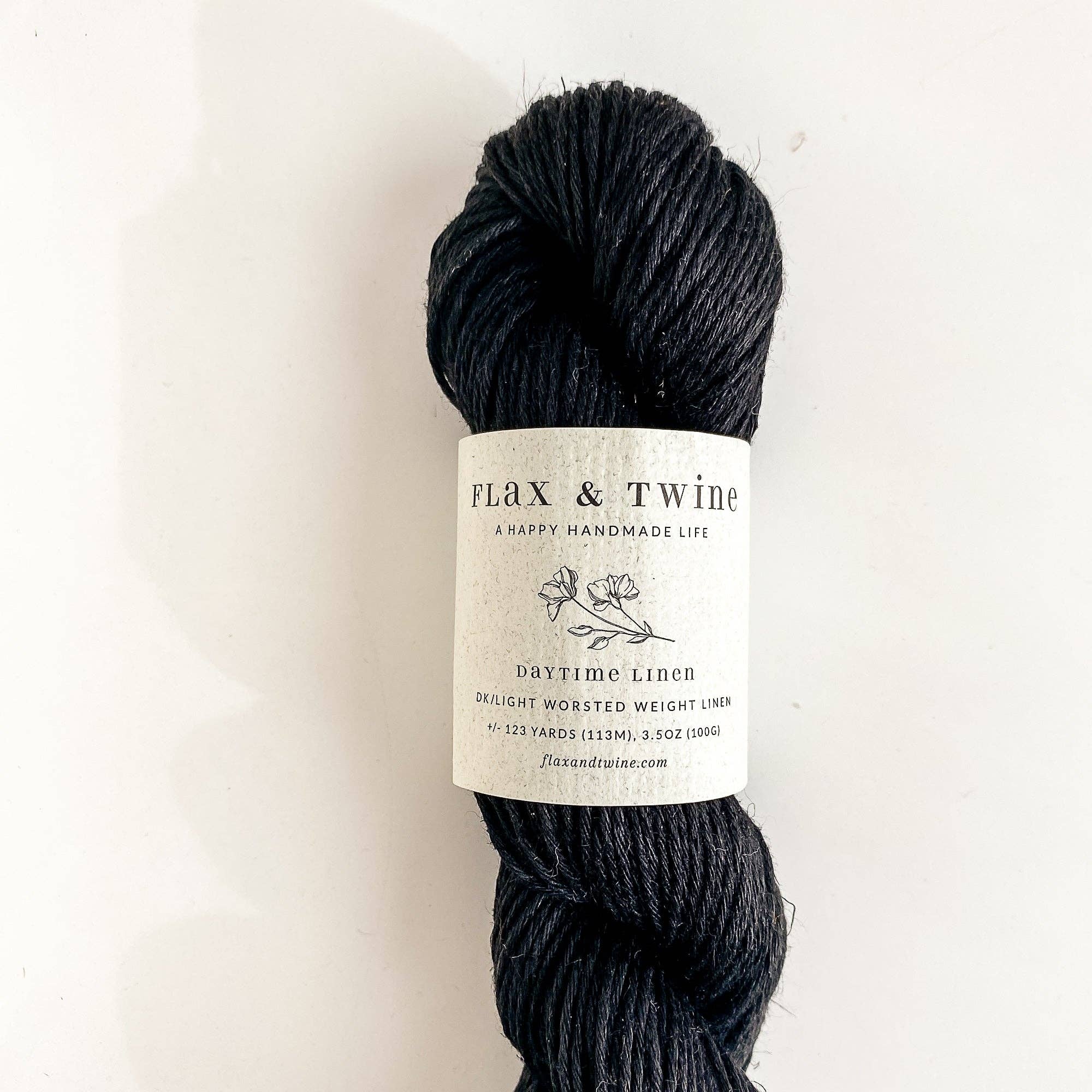 Ball of Flax & Twine Daytime Linen yarn in dark gray with a label on a light background