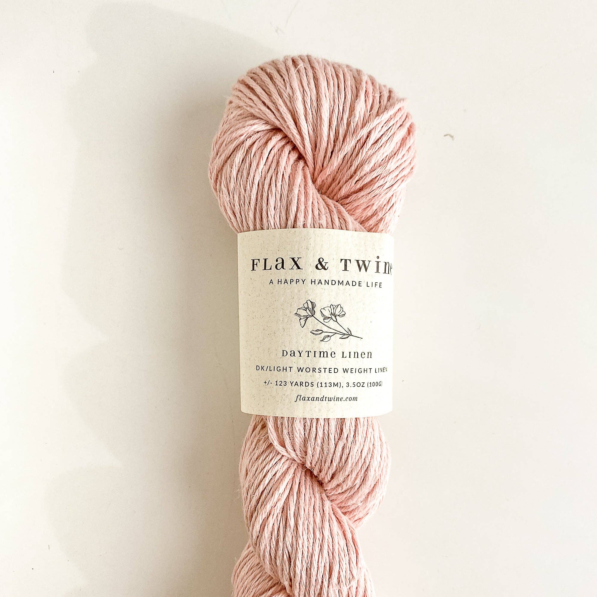 Ball of Flax & Twine Daytime Linen yarn in pink with a label on a light background