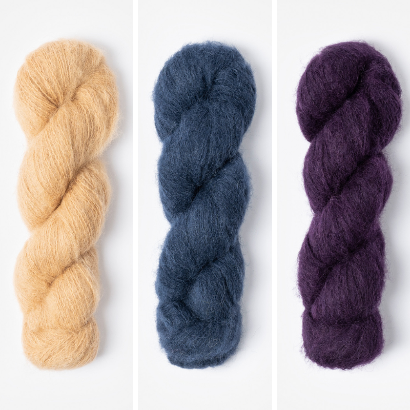 Three skeins of yarn in for the Amsterdam Wrap beige, blue, and purple on a white background