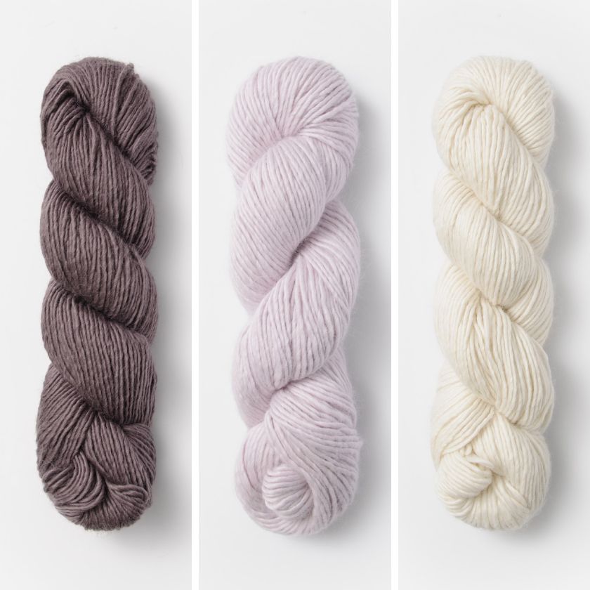 Three skeins of yarn for the Bianca Wrap in brown, pink, and cream on a white background