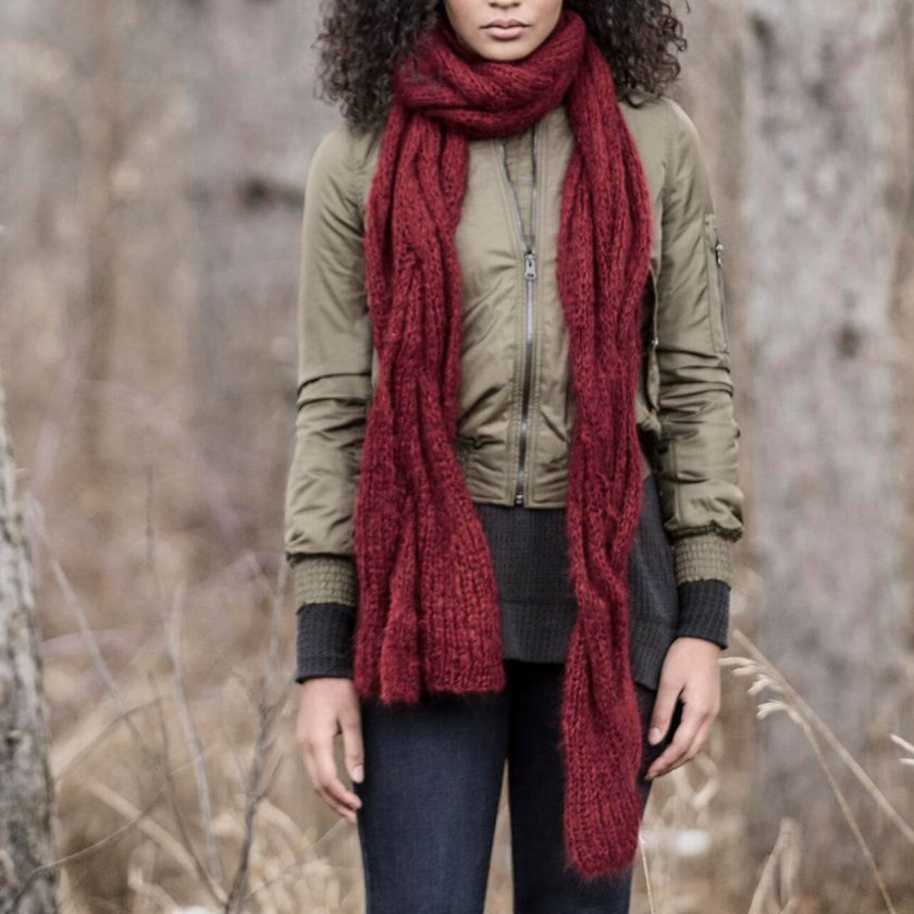 Person wearing a Candied Apple Callaway Cable scarf made from Brushed Suri yarn and green jacket in a forest setting