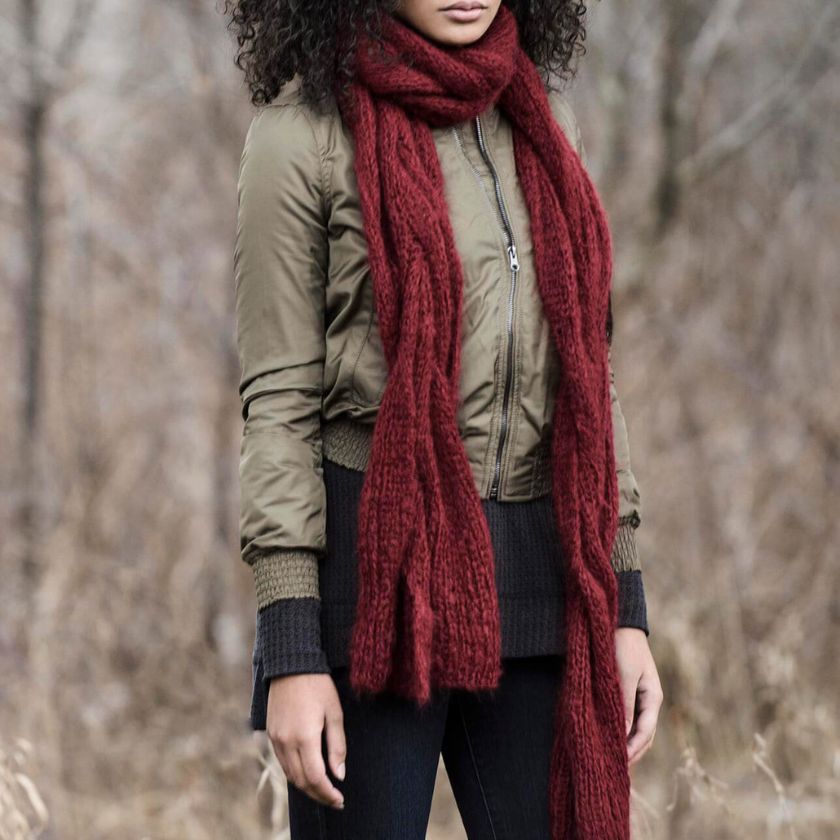 Person wearing a Candied Apple Callaway Cable scarf made from Brushed Suri yarn and green jacket in a forest setting