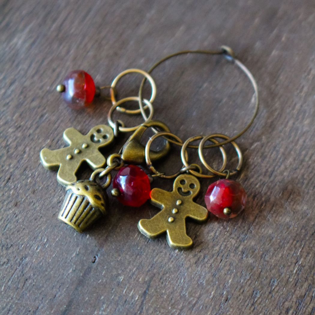 Decorative stitch markers with winter themed charms on a wooden surface.