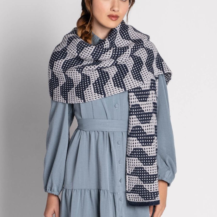 Woman wearing a blue dress and patterned knitted Market Street wrap against a gray background
