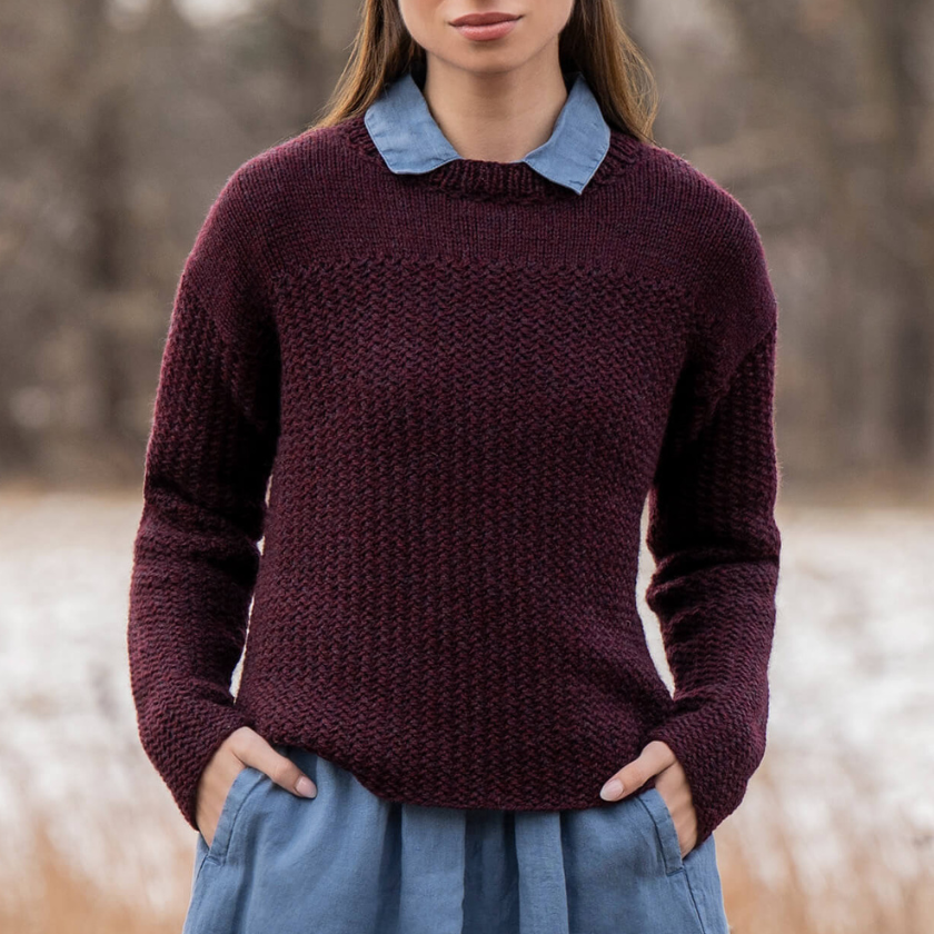 Person wearing a maroon Park Avenue pullover with a blue collar and blue jeans in a blurred outdoor setting