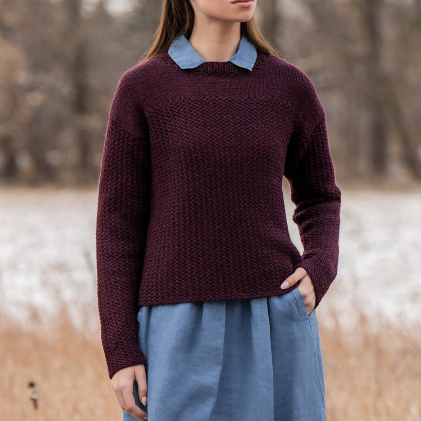 Person wearing a maroon Park Avenue pullover with a blue collar and blue pants in a natural setting.