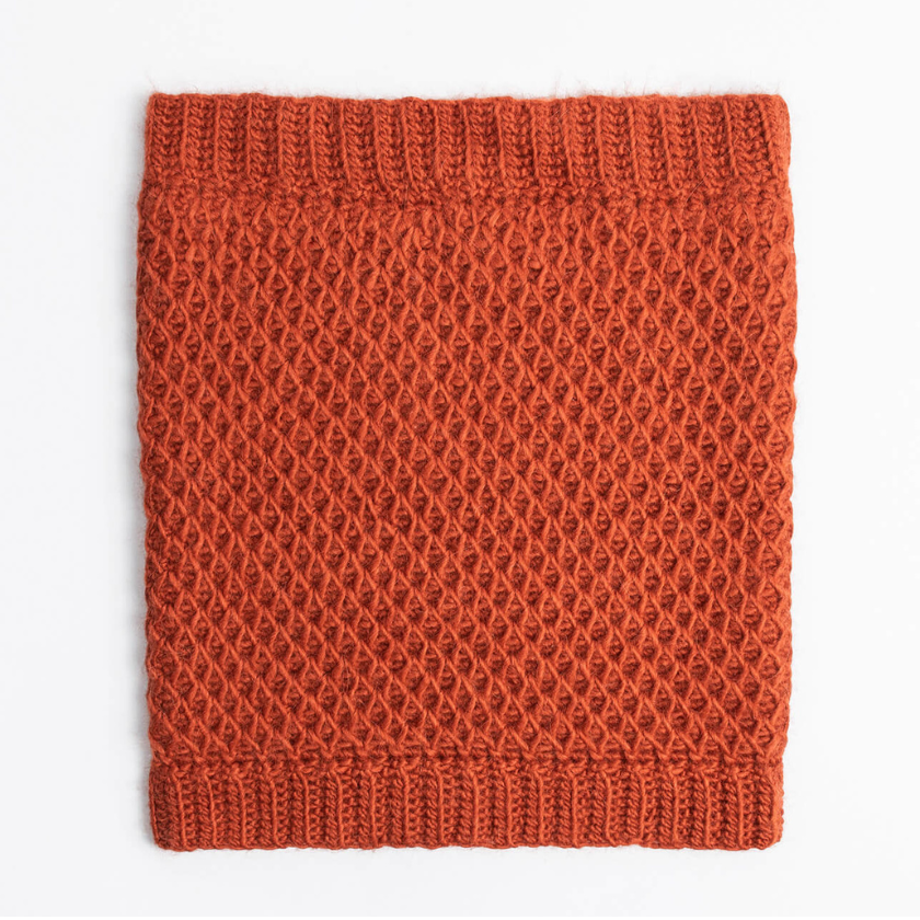 Flat lay of the Serene Sunset Cowl in the Autumn colorway, showcasing the smock stitch texture and ribbed edging in Blue Sky Fibers Suri Merino. The Dizzy Knitter