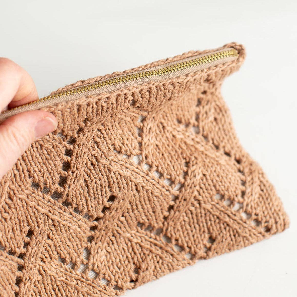 Brown knitted Rowan pouch with a gold zipper held by a hand on a light background