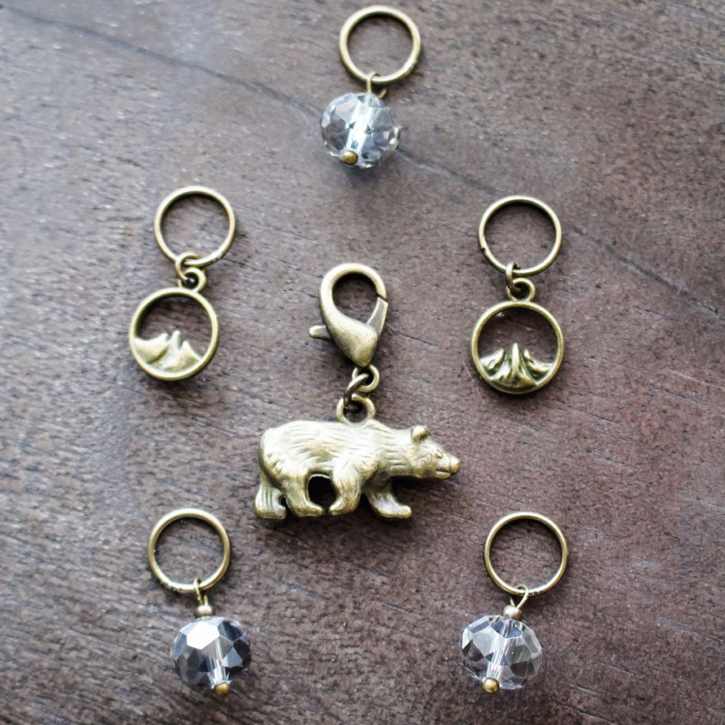 Set of bronze stitch markers with bear and crystal designs on a wooden surface
