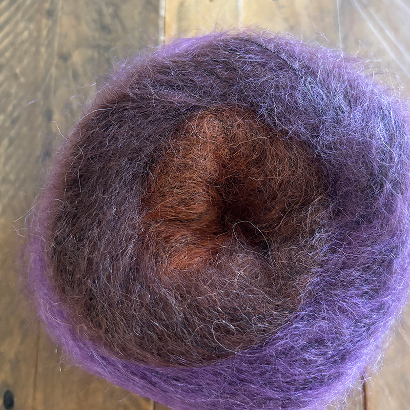 Ball of Poema Mohair yarn in Berry, Maroon, and Umber on a wooden surface