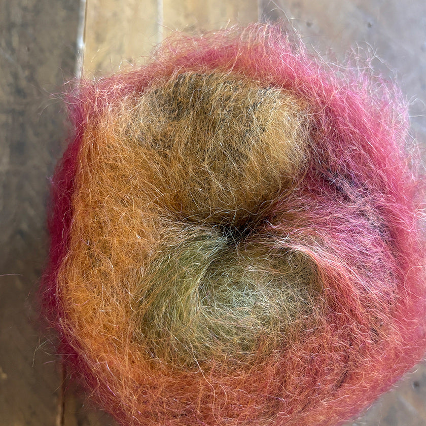 Ball of Poema Mohair yarn in Brick, Orange, and Umber Moss on a wooden surface