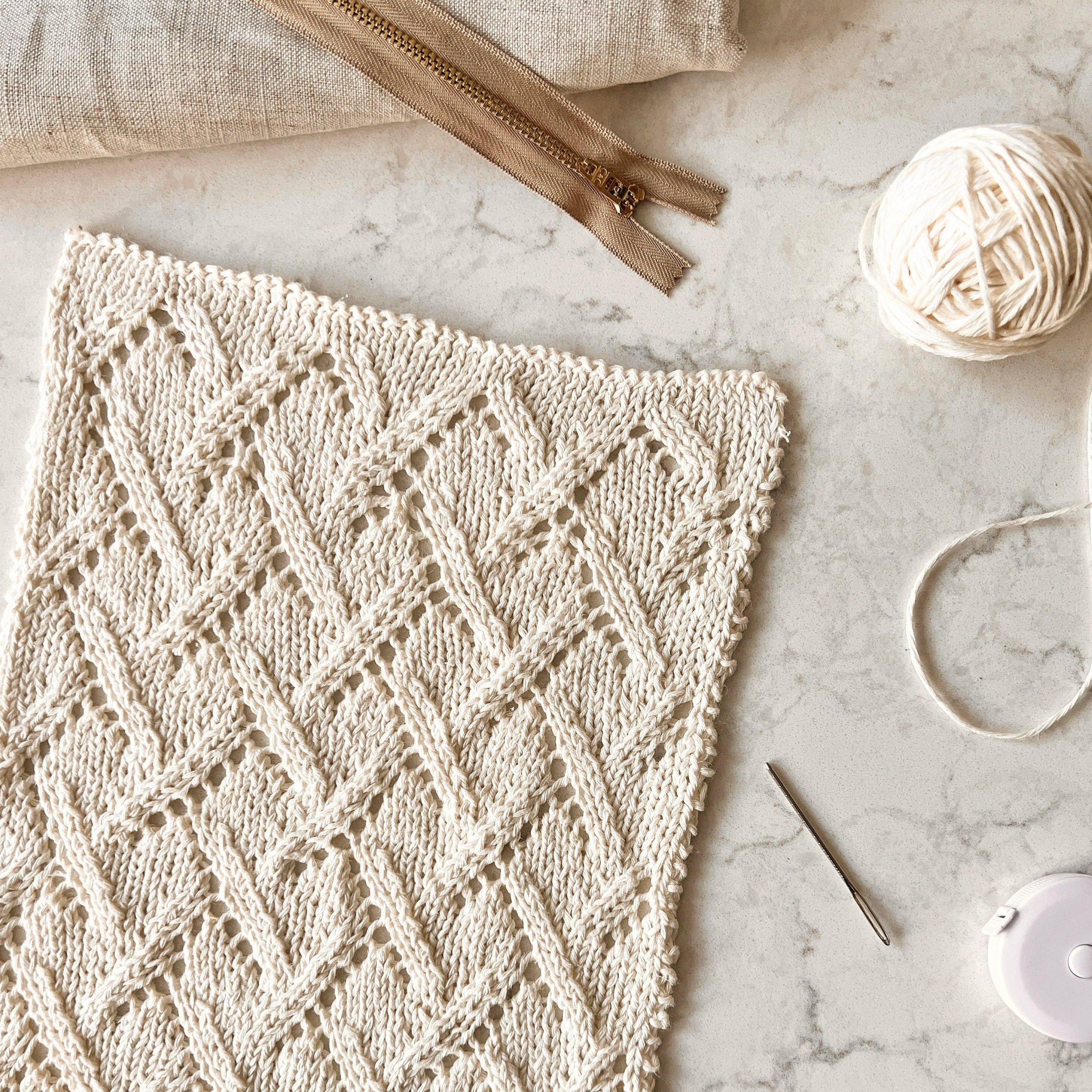 Knitted fabric with a diamond pattern on a marble surface with yarn and knitting tools.