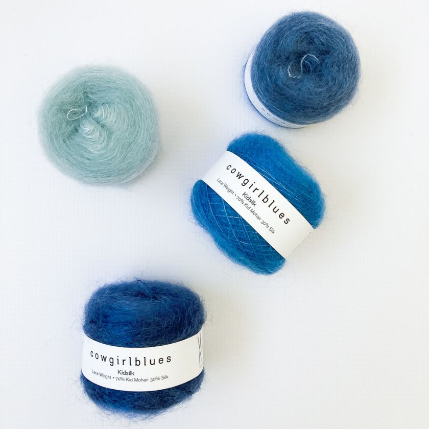 Three skeins of yarn with 'cowgirlblues' labels for the Cobweb Shawl on a white background