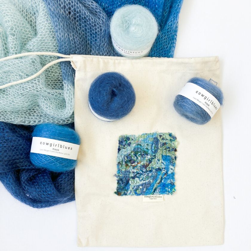 Blue yarn balls and fabric bag for the Cowbeb shawl knitting kit on a white background with 'cowgirlblues' labels.