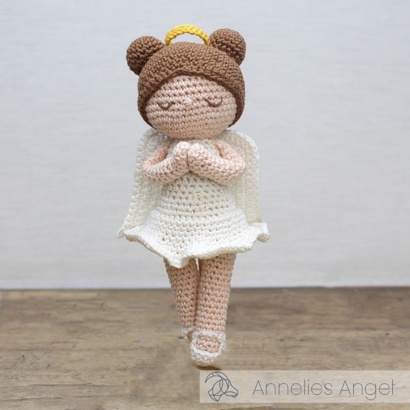 Crocheted angel doll with brown hair bun, halo, and white dress on a wooden surface.