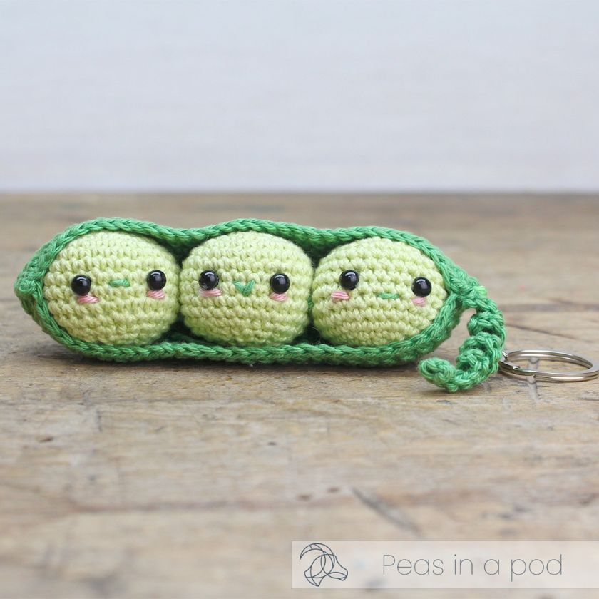 Crocheted keychain shaped like peas in a pod on a wooden surface with 'Peas in a pod' branding.