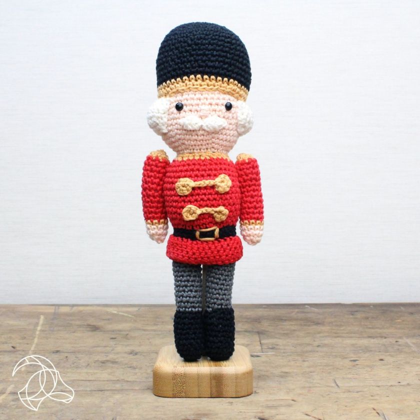 Crocheted toy soldier figure kit on a wooden stand with a plain background