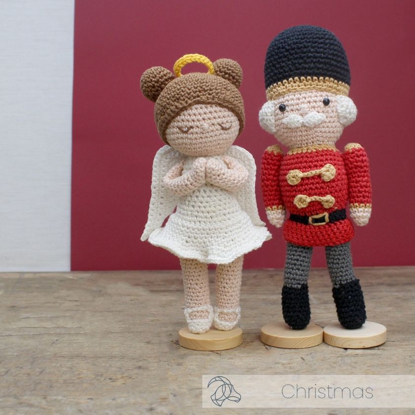 Crocheted angel and nutcracker figures made from Hardicraft kits on wooden stands with a red background.