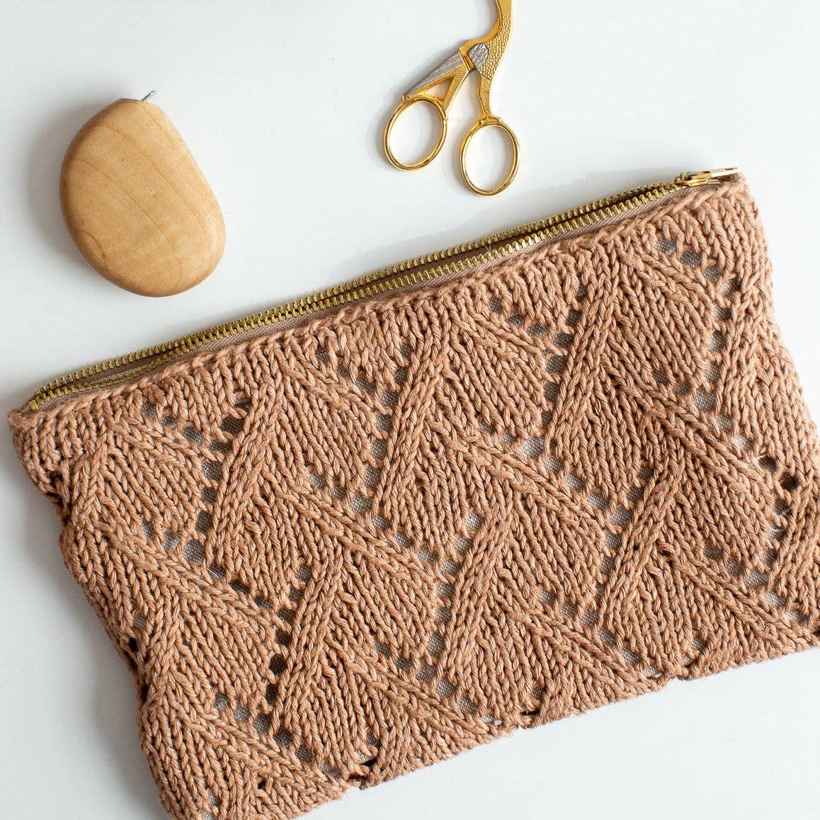 Knitted Rowan pouch with a geometric pattern, accompanied by a wooden object and gold scissors on a light background.