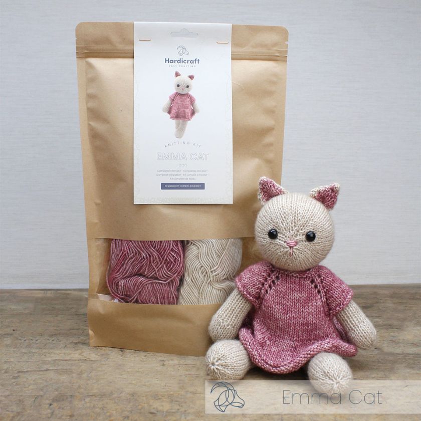 Knitted Emma Cat toy with pink dress and knitting kit on a wooden surface.