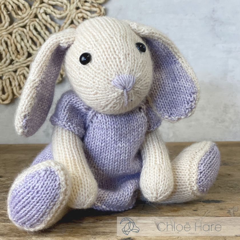 Knitted Amigurumi Chloe Hare in a purple dress on a wooden surface