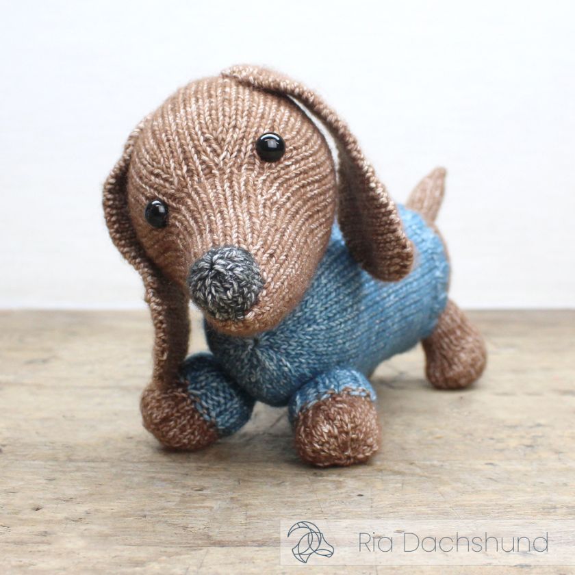 Knitted dachshund toy from Amigurumi wearing a blue sweater on a wooden surface