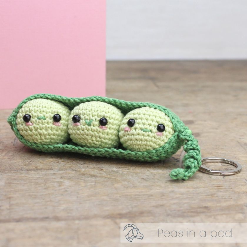 Crocheted keychain shaped like peas in a pod on a wooden surface with a pink background.
