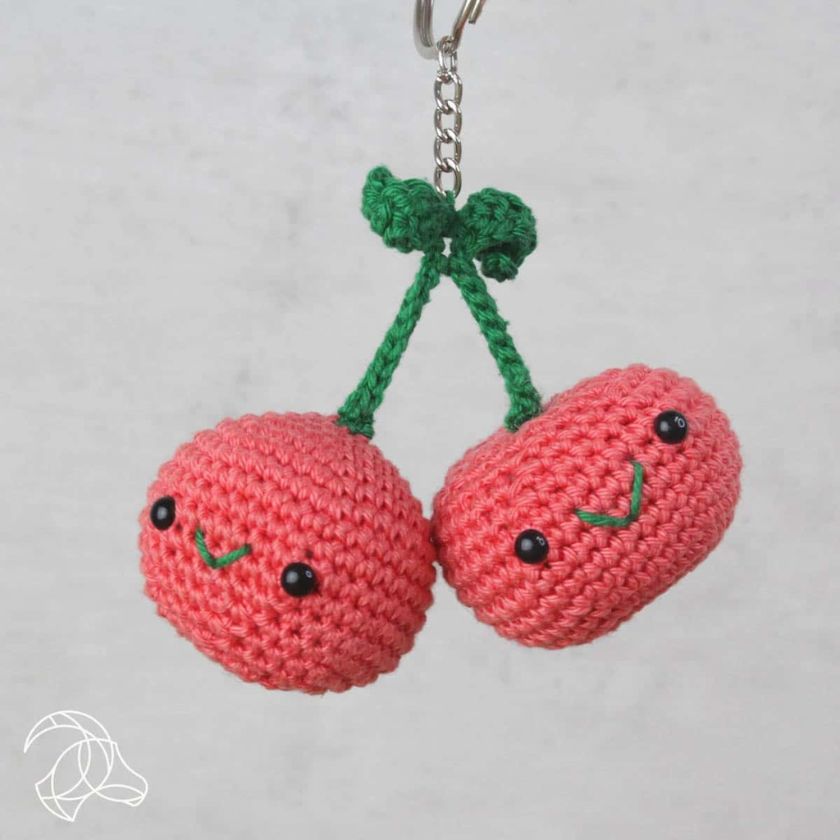 Crocheted cherry keychain with a green stem on a light gray background