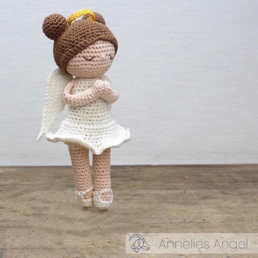 Crocheted project kit angel doll with brown hair bun and white dress on a wooden floor.