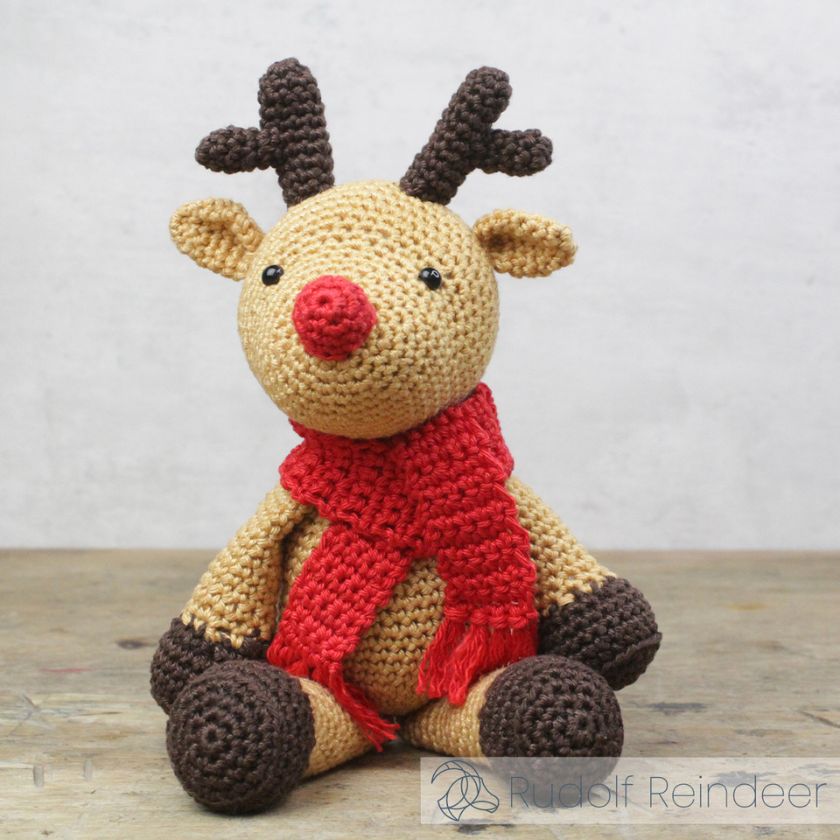 Crocheted reindeer toy with a red scarf on a wooden surface.