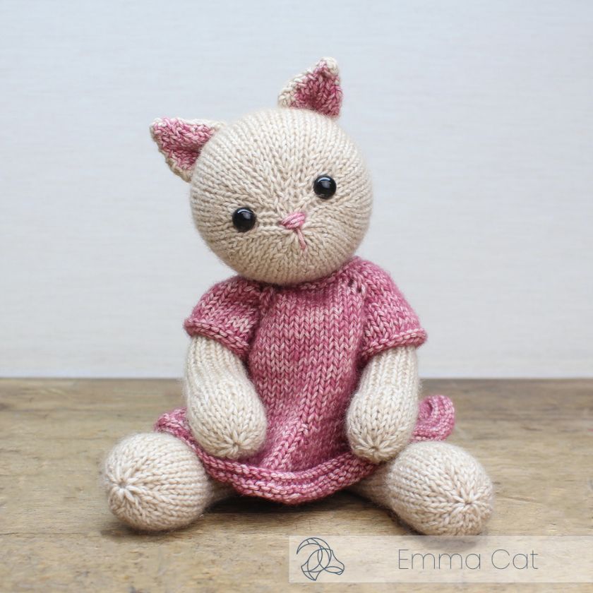 Knitted Emma Cat toy with pink dress by Amigurumi on a wooden surface.