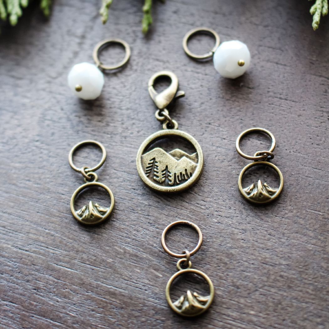 Bronze stitch markers with mountain designs on a wooden surface