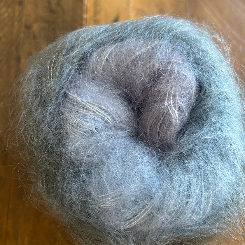 Ball of Poema Mohair yarn in Sage, Aqua, and Lavender on a wooden surface