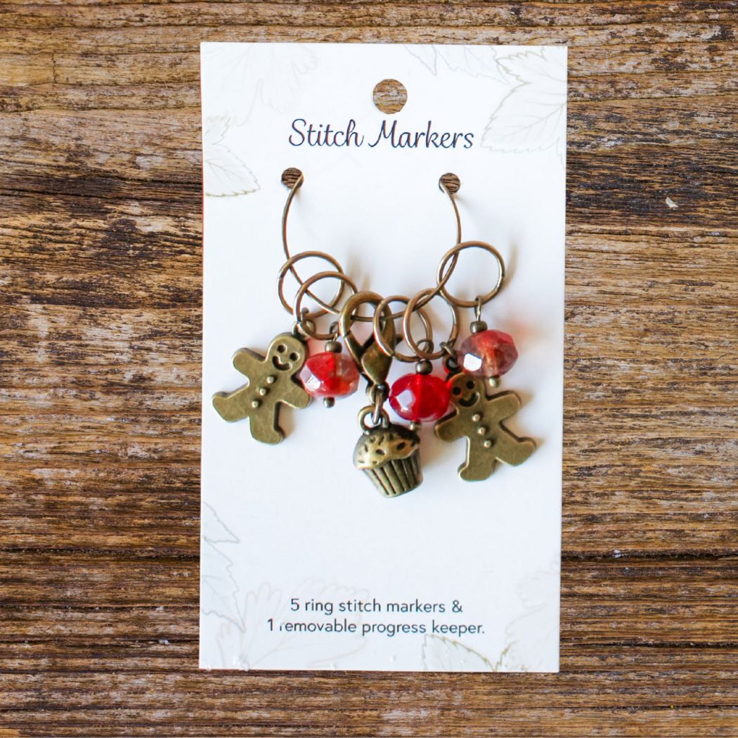 Set of stitch markers with holiday charms on a card, placed on a wooden surface.