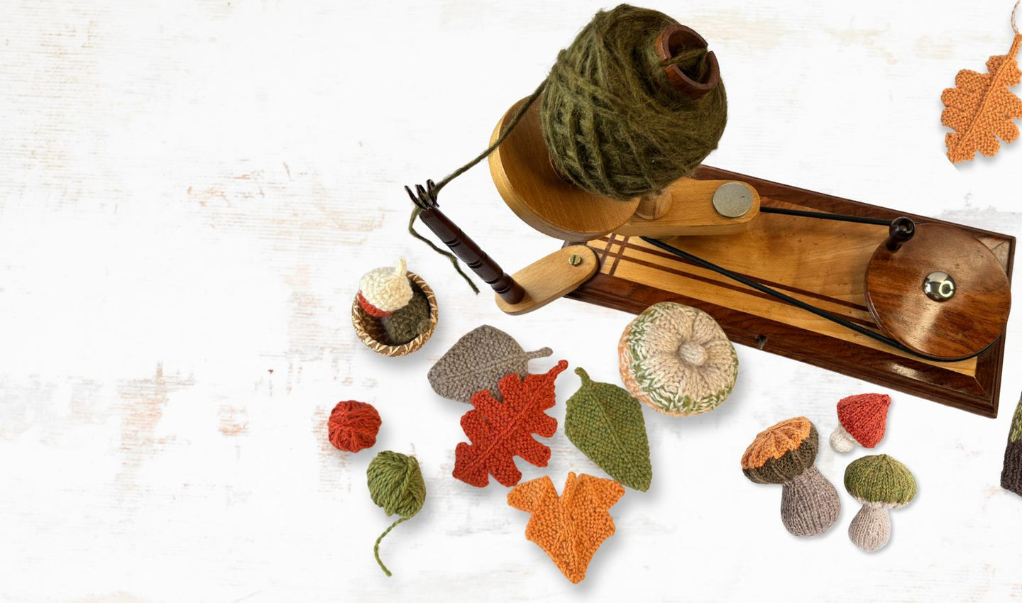Autumn-themed knitting items including a hat, leaves, and a small shovel on a textured white background