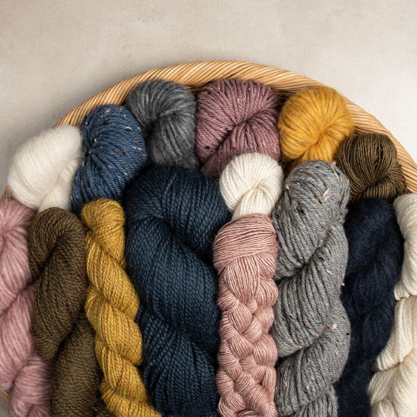Assorted skeins of yarn in various colors arranged in a woven basket.
